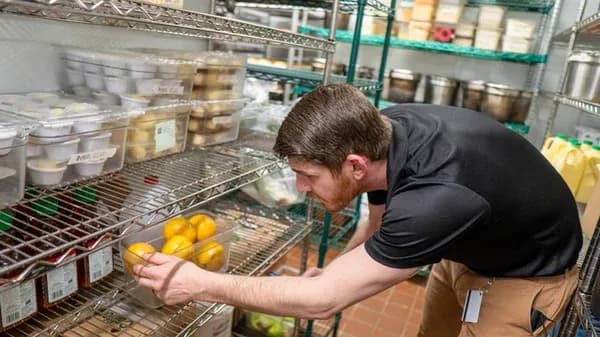Chef checking labeled containers of fresh produce on organized shelving in a food storage room